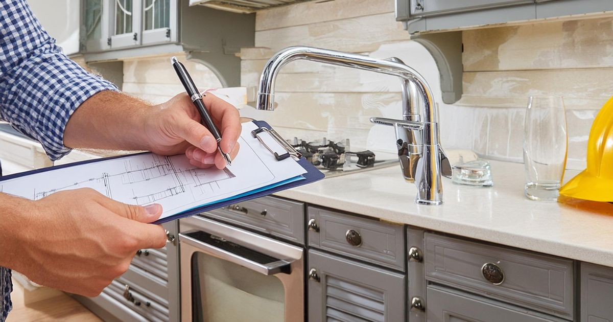 Man taking notes on a clipboard in front of a kitchen sink.