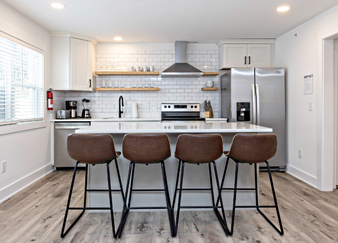 A kitchen with a white countertop and brown chairs

Description automatically generated