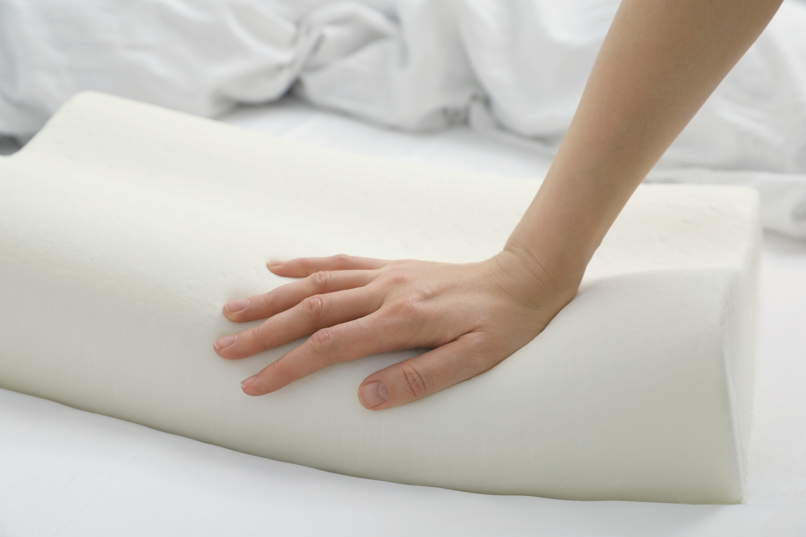 A hand pressing down on a memory foam pillow made with polyurethane