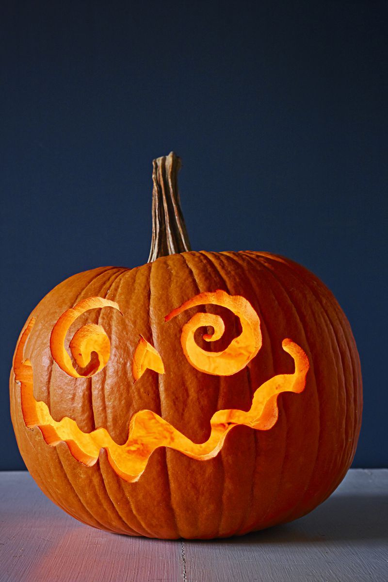 pumpkin carving ideas, pumpkin carved with swirly eyes and a swirly smilemn