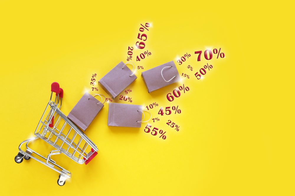 A miniature shopping cart and shopping bags and discount icons falling out of it 