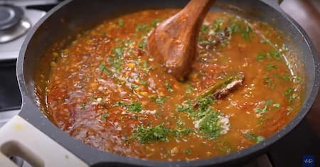 A pinch of garam masala, chopped coriander, and butter being added to the dal mixture in a pan.