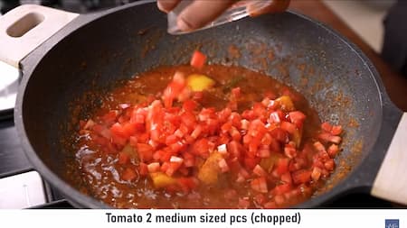 Chopped tomatoes being added to the masala mixture in a pan, ready to be cooked until soft and mushy.