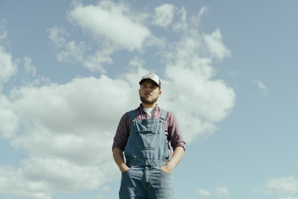Amerikanischer Farmer in einer Jeans Latzhose und Basecap vor blauem Himmel