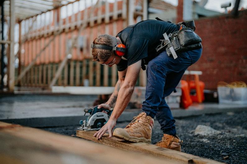 A person wearing headphones and working on a piece of wood

Description automatically generated