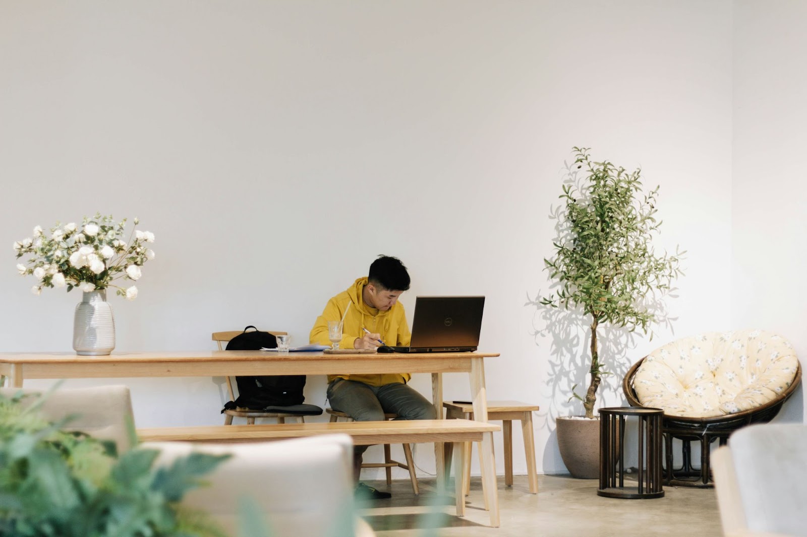 Young man working on his laptop on a long wooden table with plants