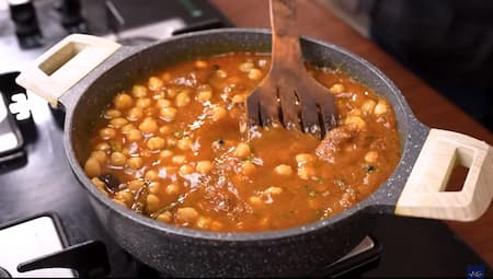 Boiled chickpeas being added to the prepared masala in a pan.
