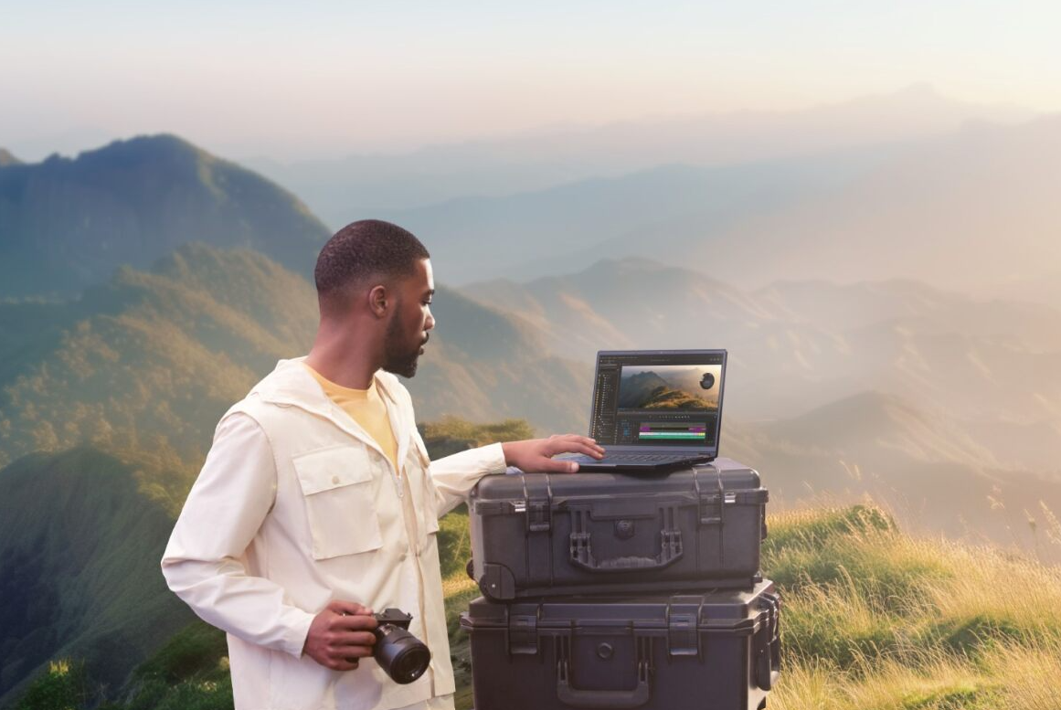 A person standing on top of a mountain with a computerDescription automatically generated