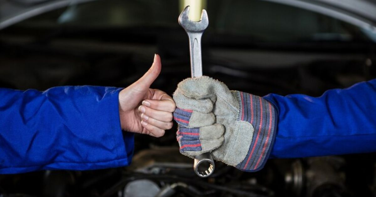 Two individuals confidently hold a wrench, displaying a thumbs up gesture, indicating success or approval.