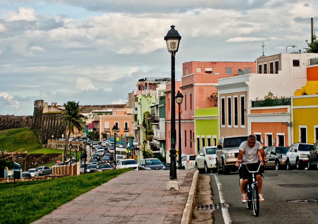 a man cycling on a street pastel-colored buildings.