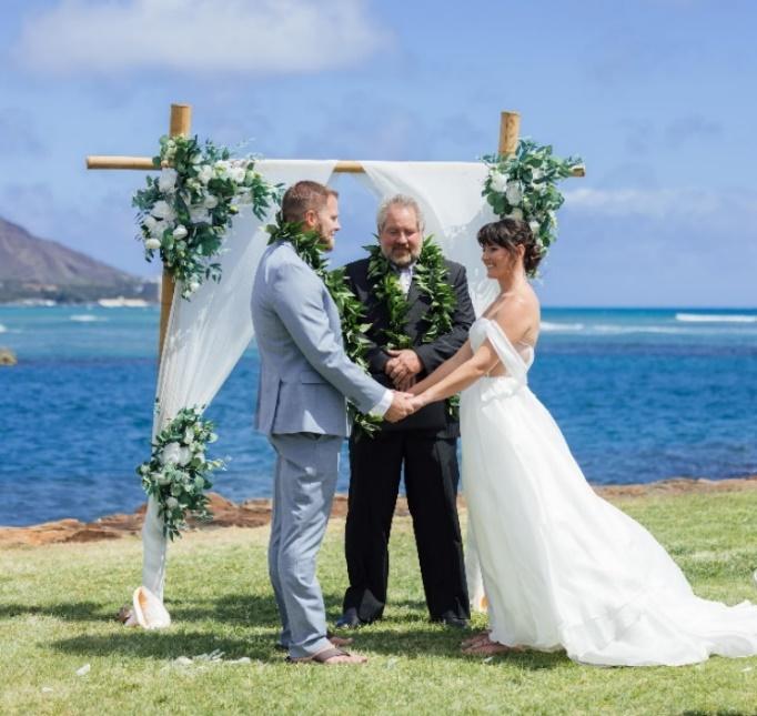 A couple holding hands and standing under a wedding arch

Description automatically generated