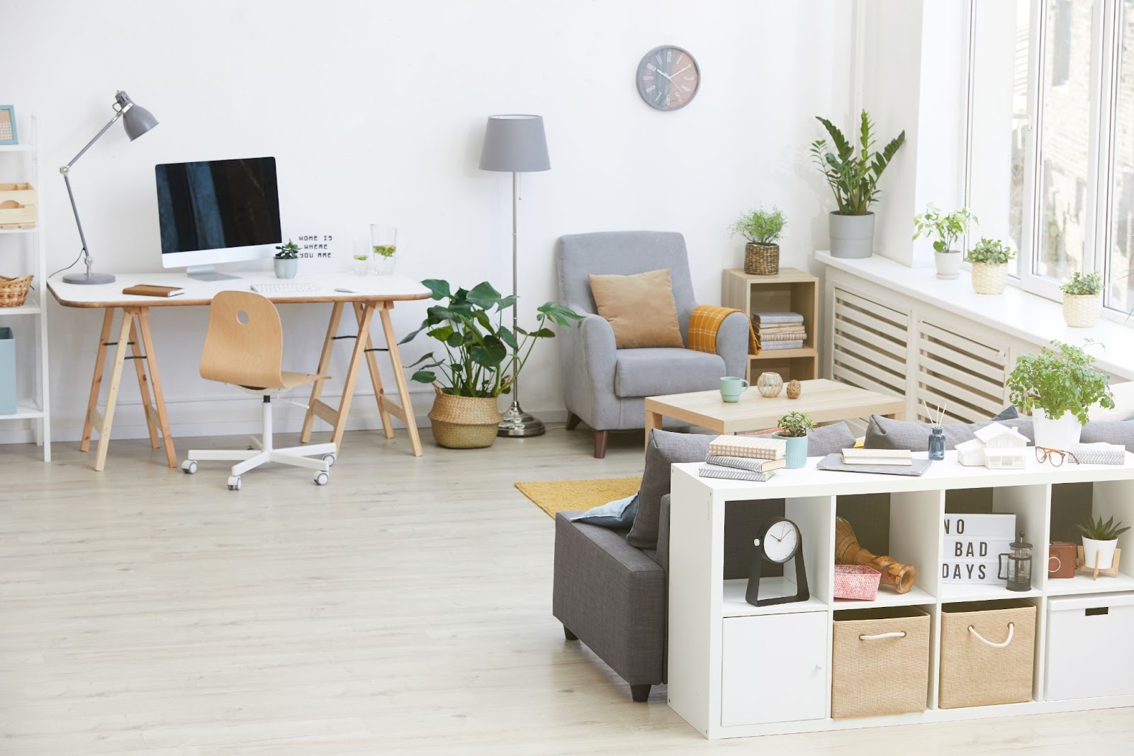 A white and gray themed living room with multi-functional spaces, featuring sleek and modern furniture such as open bookshelves, slatted cabinets, a table, lounge chairs, and tall lamps.