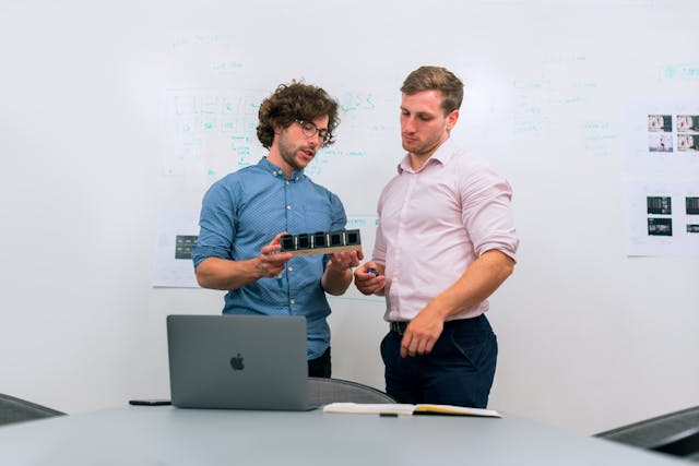 Two men standing in front of a laptop, engaged in a collaboration or consultation