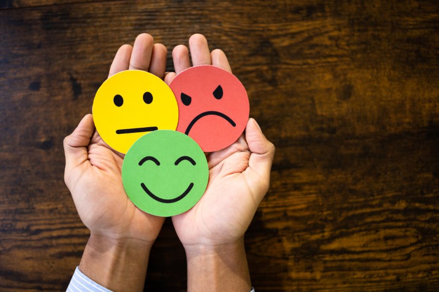 Hands holding happy, neutral, and sad face emoticons on wooden background.