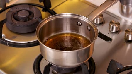 Adding loose tea leaves, crushed ginger, cloves, and a cardamom pod to boiling water.