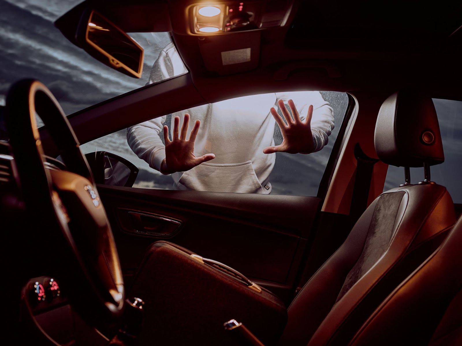 A person with hands pressed against a car window, viewed from the inside of a vehicle, creating a dramatic and urgent scene