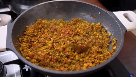 Cooked dal being mixed with the tempering mixture in a pan.