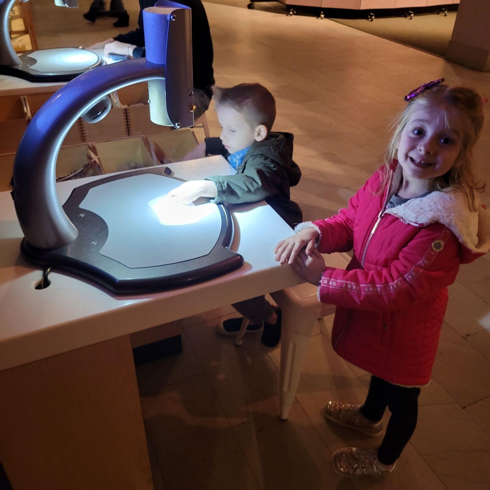 A child and child standing next to a microscopeDescription automatically generated