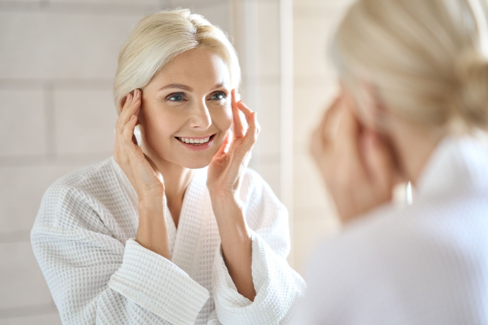 A smiling middle-aged woman happily touches her smoother facial skin.