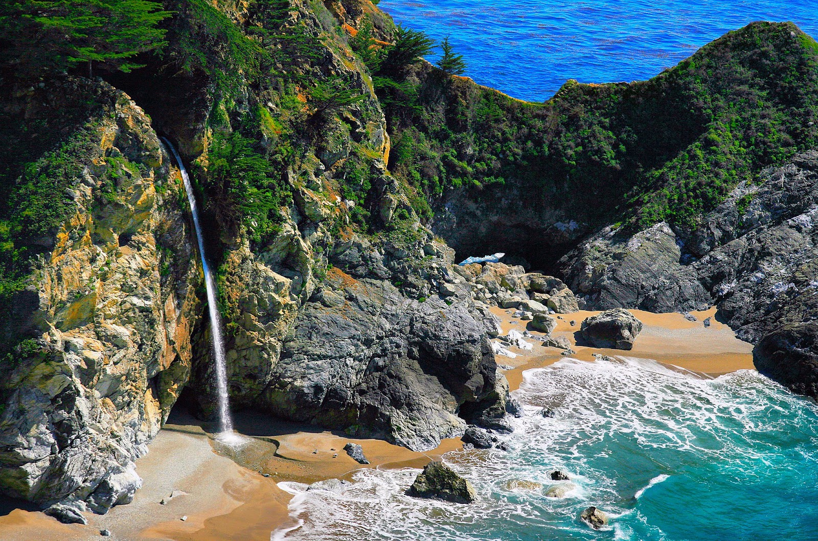 Massive lush cliffs, majestic waterfall and clear water in the beach.