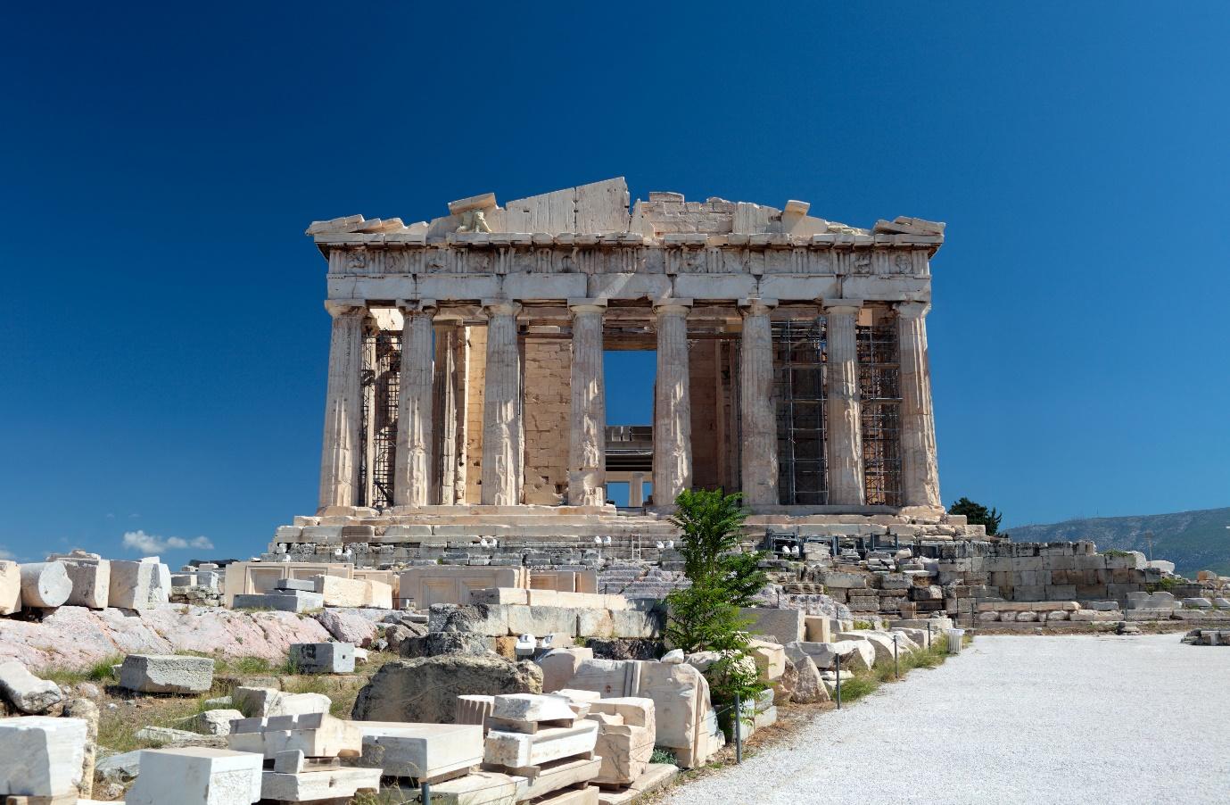 A stone building with columns with Parthenon in the background

Description automatically generated