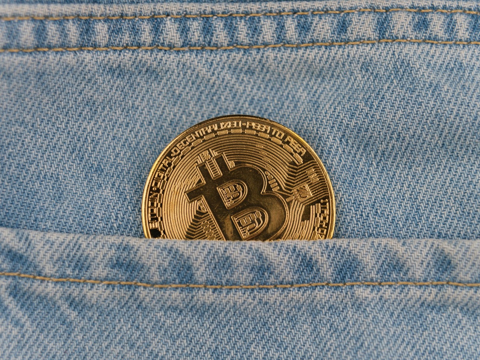 A gold Bitcoin coin partially visible in the front pocket of blue jeans