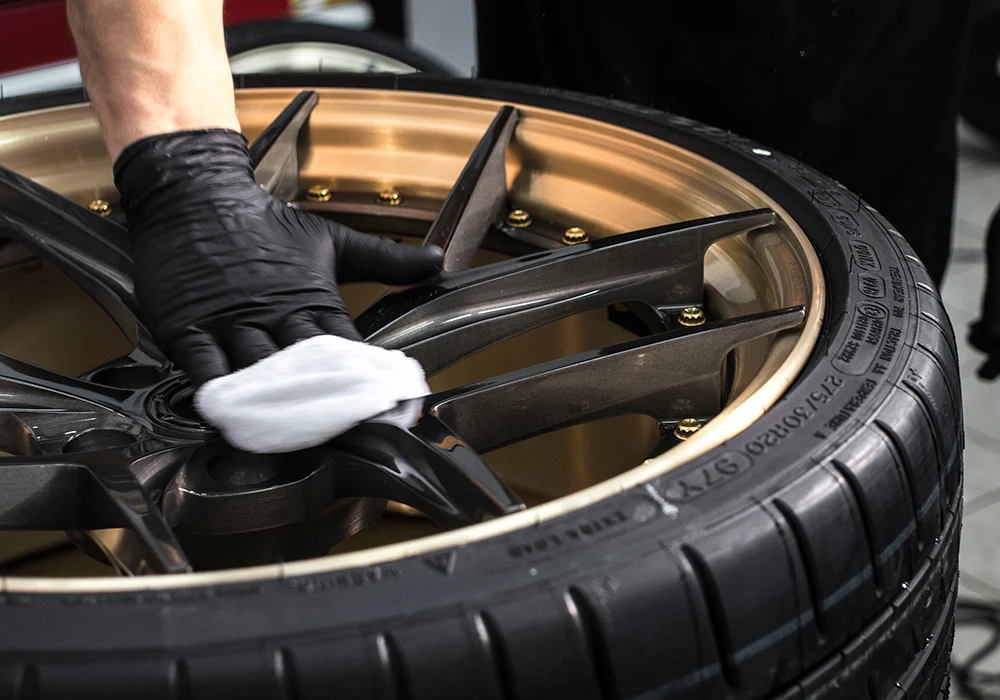 Close-up view of a car wheel as a ceramic coating is applied. The focus is on the wheel's intricate design and the coating process, which ensures a protective, glossy finish.