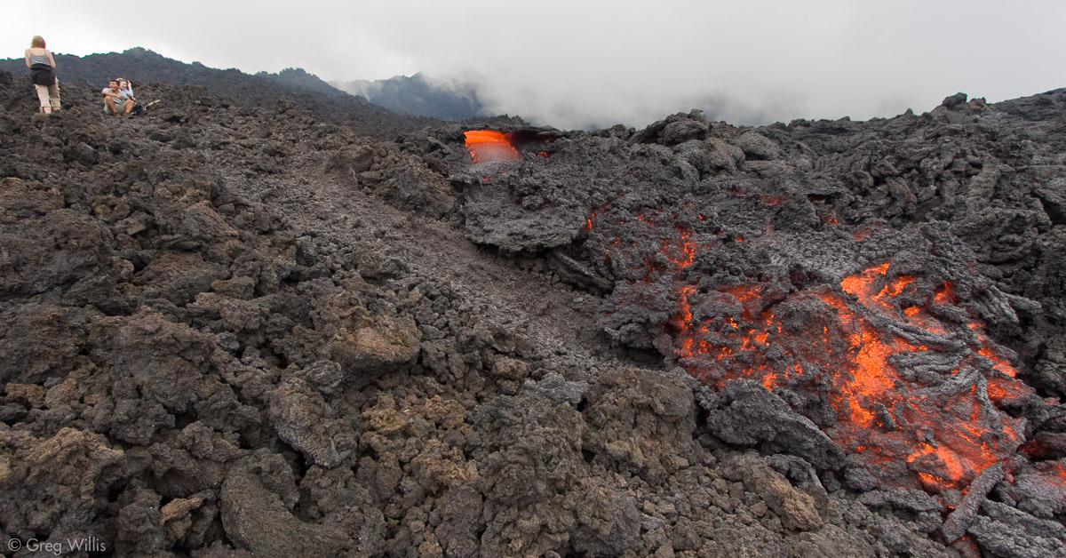 a volcanic outburst that sent lava streaming down the stony mountainside. The sky is being filled with pollutants and smoke from the Pacaya Volcano. A couple is having fun next to the lava.