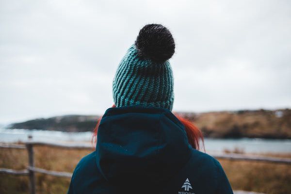 Frau an der Nordseeküste mit Kapuzenjacke und Wollmütze mit einer Bommel aus Kunstfell.