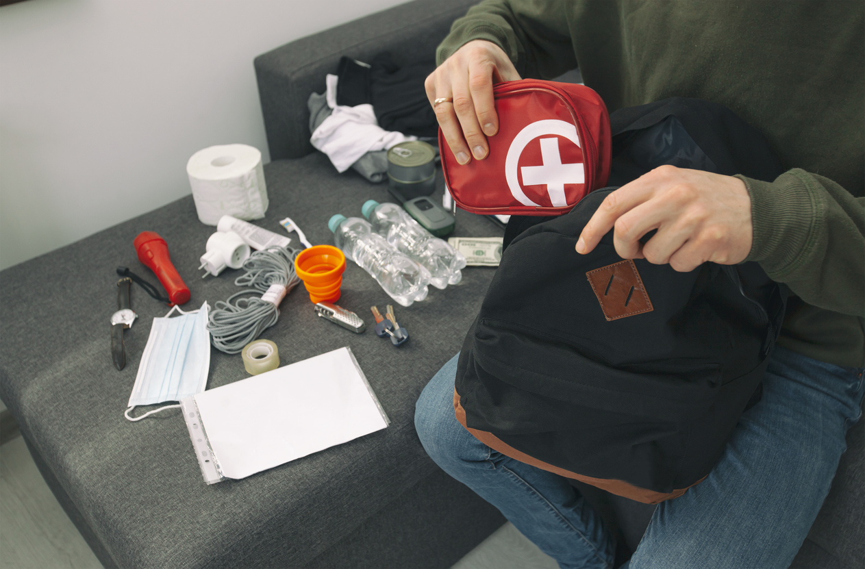 A person packs an emergency go bag with a first aid kit, water bottles, documentation, a flashlight, and other supplies.