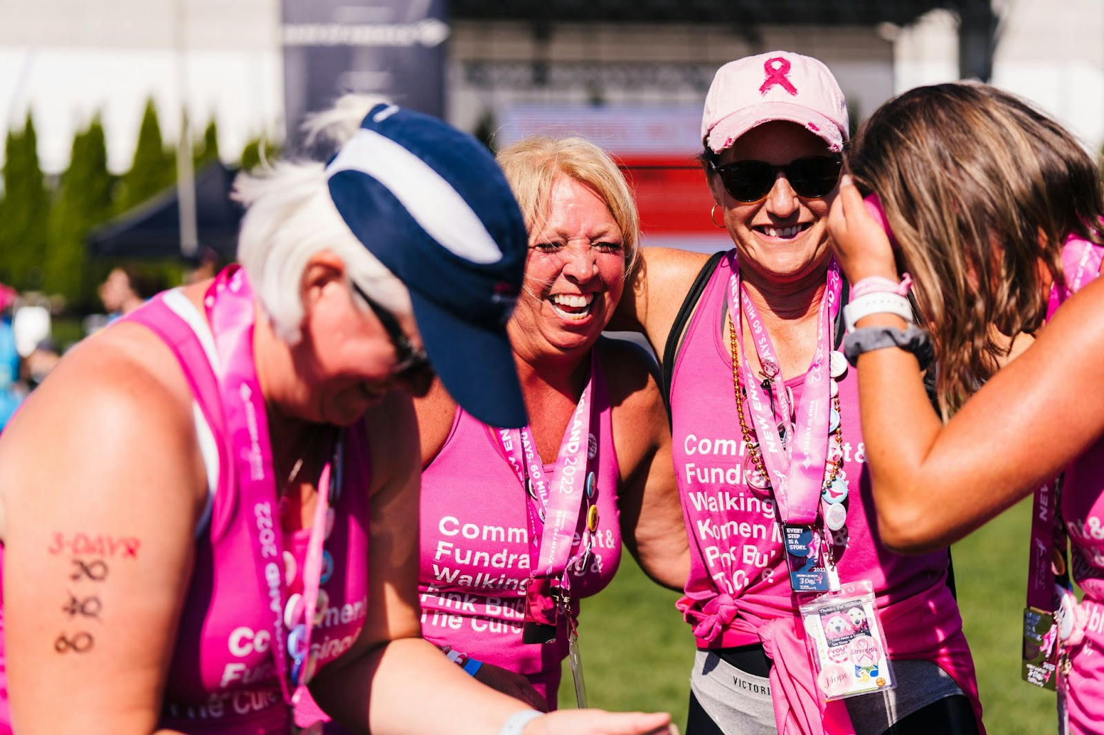 A group of women wearing matching pink printed tank tops, embracing at a breast cancer awareness walk, put on by the Susan G. Komen foundation. 