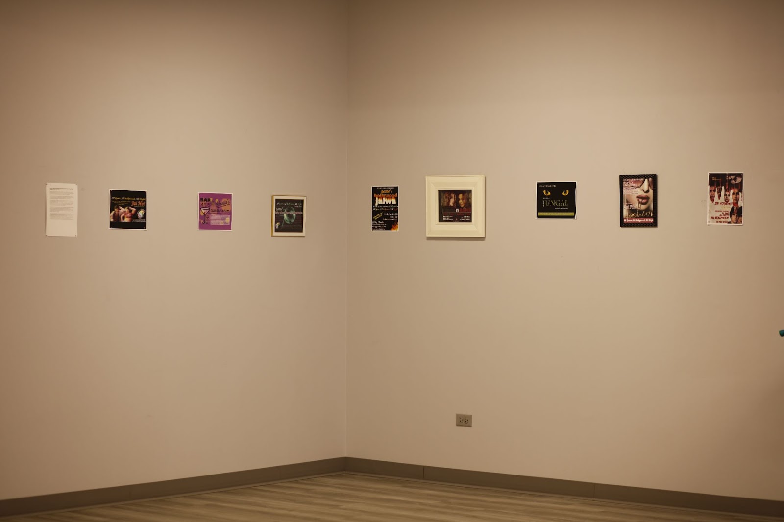 Image: Installation view, People Who Came Before Us. In a horizontal row across two walls, posters advertising events and benefits are hung against a blank wall. Courtesy of South Asia Institute.