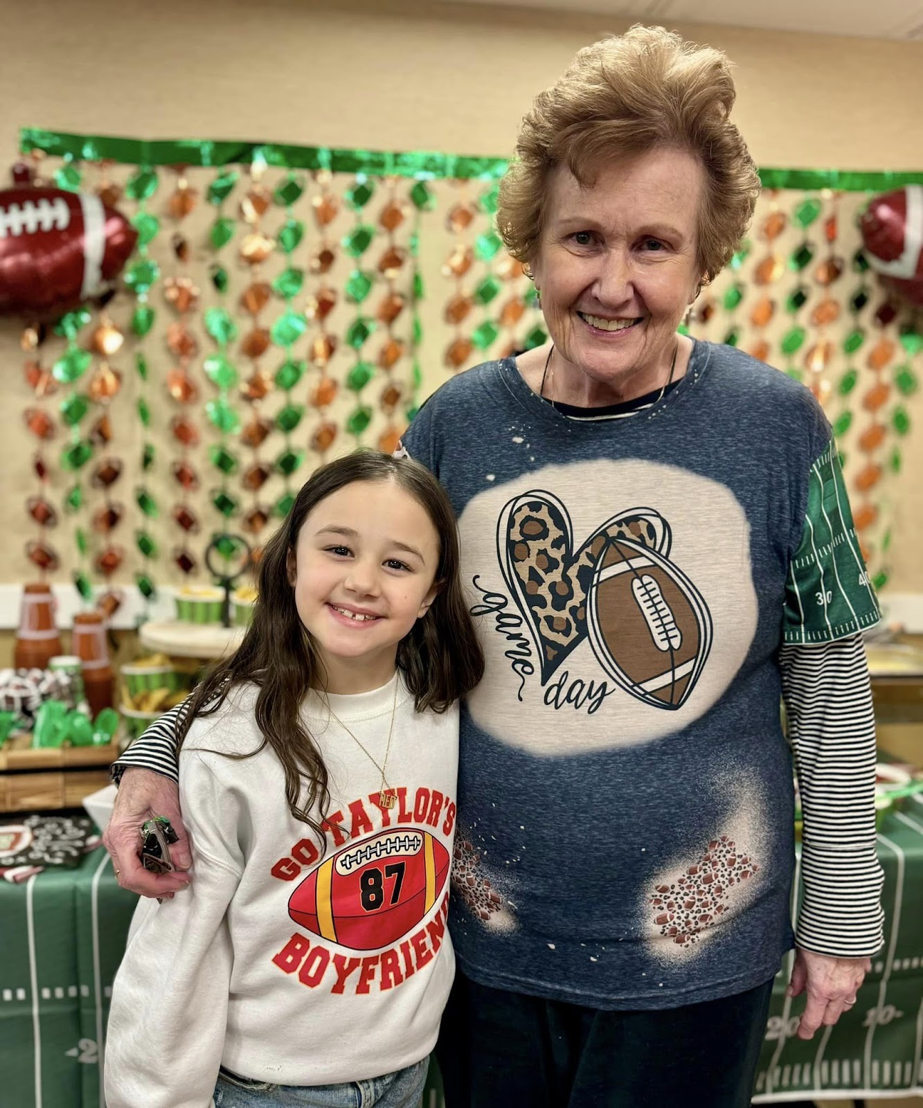 A memory care resident an elementary school-aged child smiling with football sweatshirts.