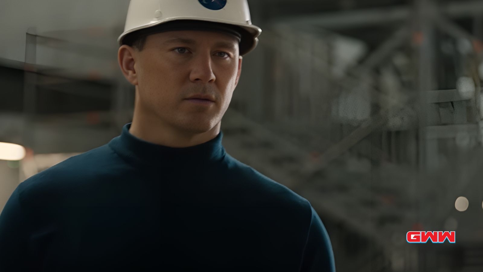 Cole in a white hard hat and blue shirt, standing in an industrial setting.