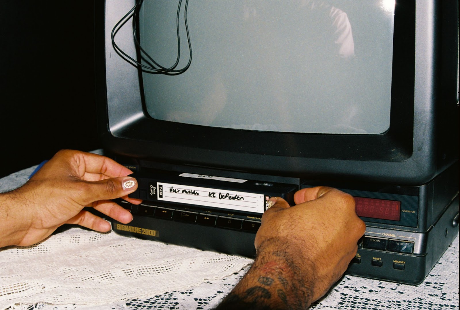 Image: A close up of Montalvo's hands inserting a videotape into a television's VCR as displayed at Montalvo’s {B/qKC}: The Volume_2 Archive Launch Party. Photo by Jade Williams.