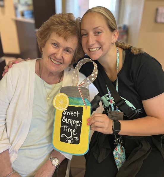 A memory care worker and a resident holding up an arts and craft creation