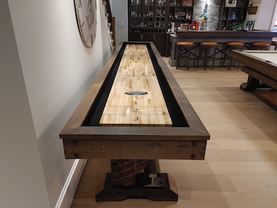 A shuffleboard in a grey basement with a bar in the background.