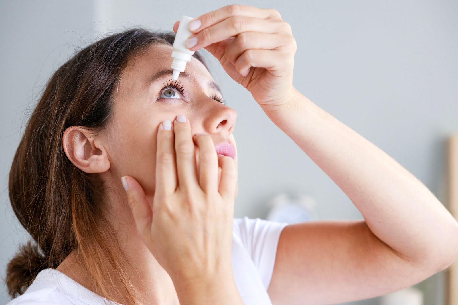 A woman pulls down her eyelid to carefully administer eye drops to relieve dry eye