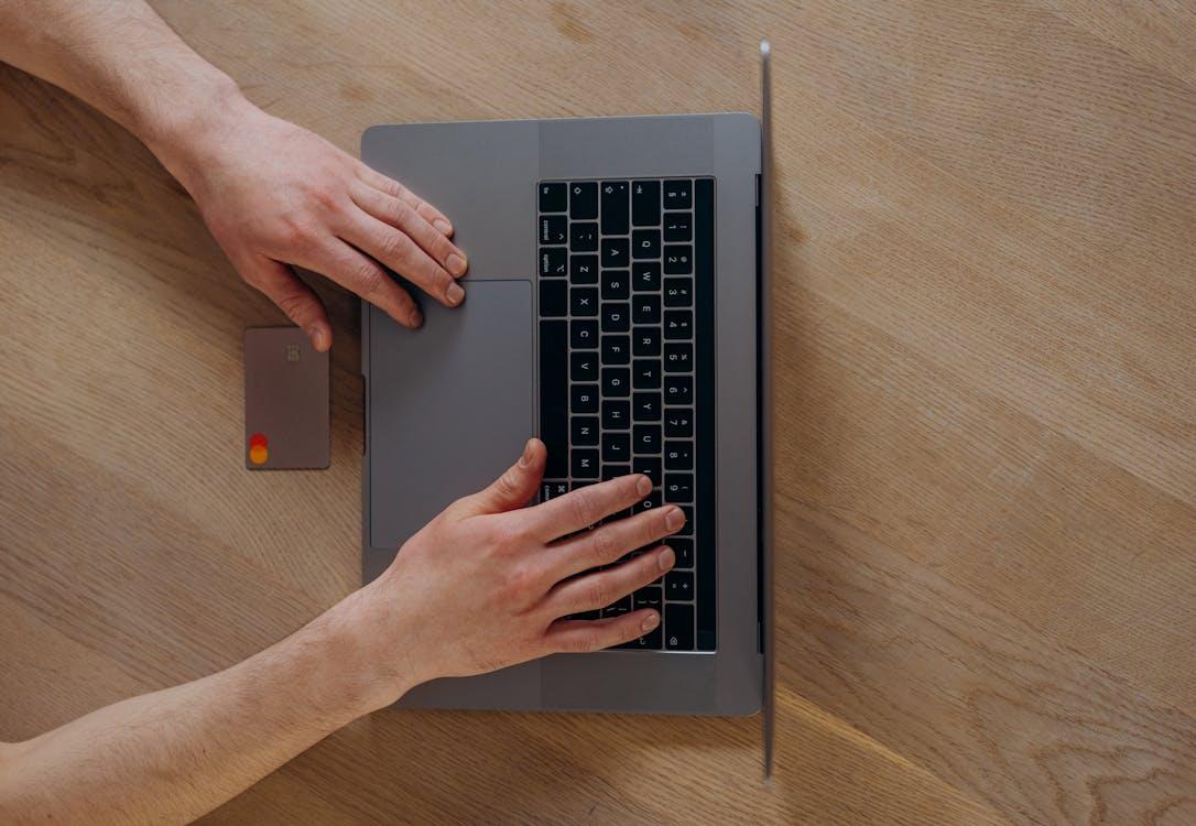 Free A Person Using a Laptop Beside a Credit Card on a Wooden Table Stock Photo