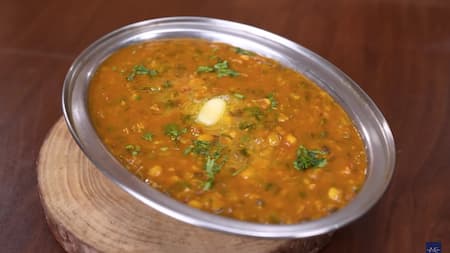 A bowl of Urad Chana Dal Tadka garnished with fresh coriander and served with hot phulkas on the side.