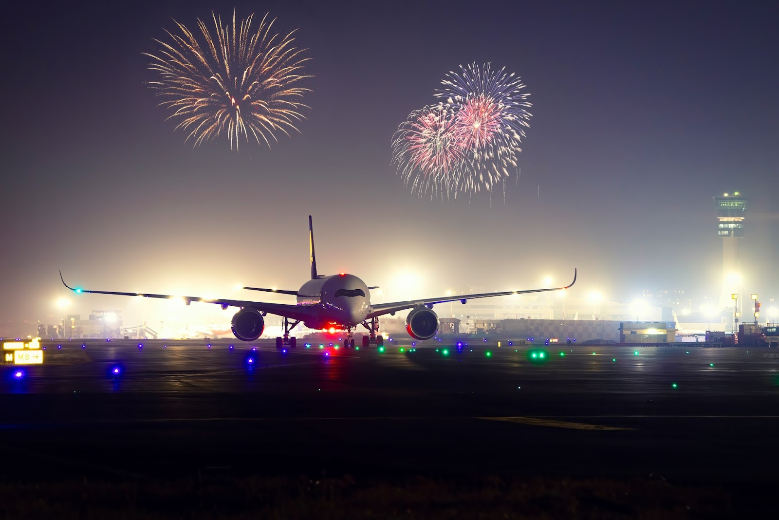 A massive jet airplane just landed in the runway with fireworks as a background.