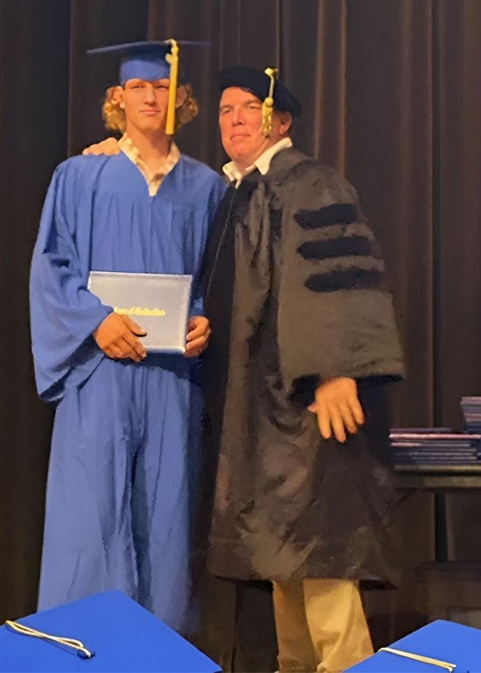 A person in a graduation gown and cap standing next to a person in a graduation gown

Description automatically generated