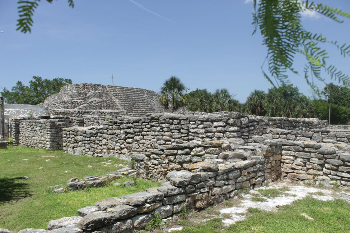 A stone wall with a stone fence outdoors, set against a backdrop of a clear sky and trees. It gives a sense of ancient ruins and an archaeological site.