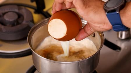 Pouring a cup of milk into the saucepan with tea and spices.