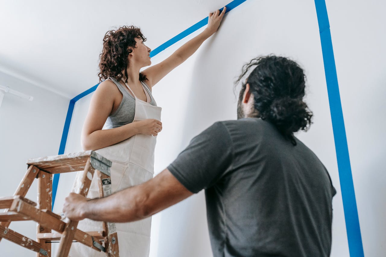 Man and woman carefully taping off sections while painting a room together.