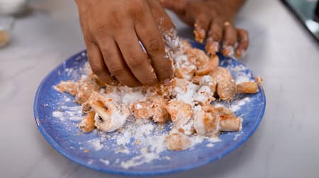 Mushrooms being coated with a flour mixture for frying.