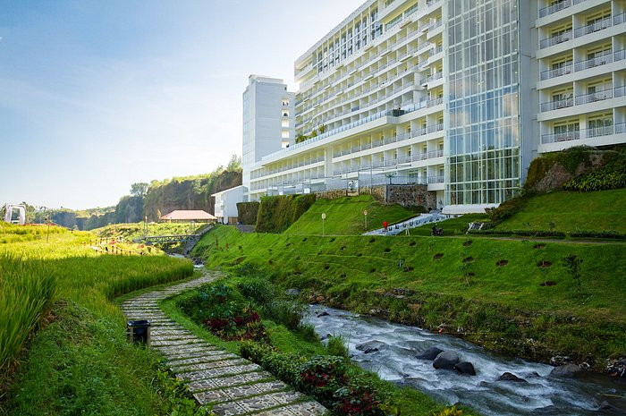 keindahan jalan setapak yang dikelilingi rumput hijau dan sungai kecil dengan latar belakang penginapan Le Eminence Puncak Hotel Convention & Resort