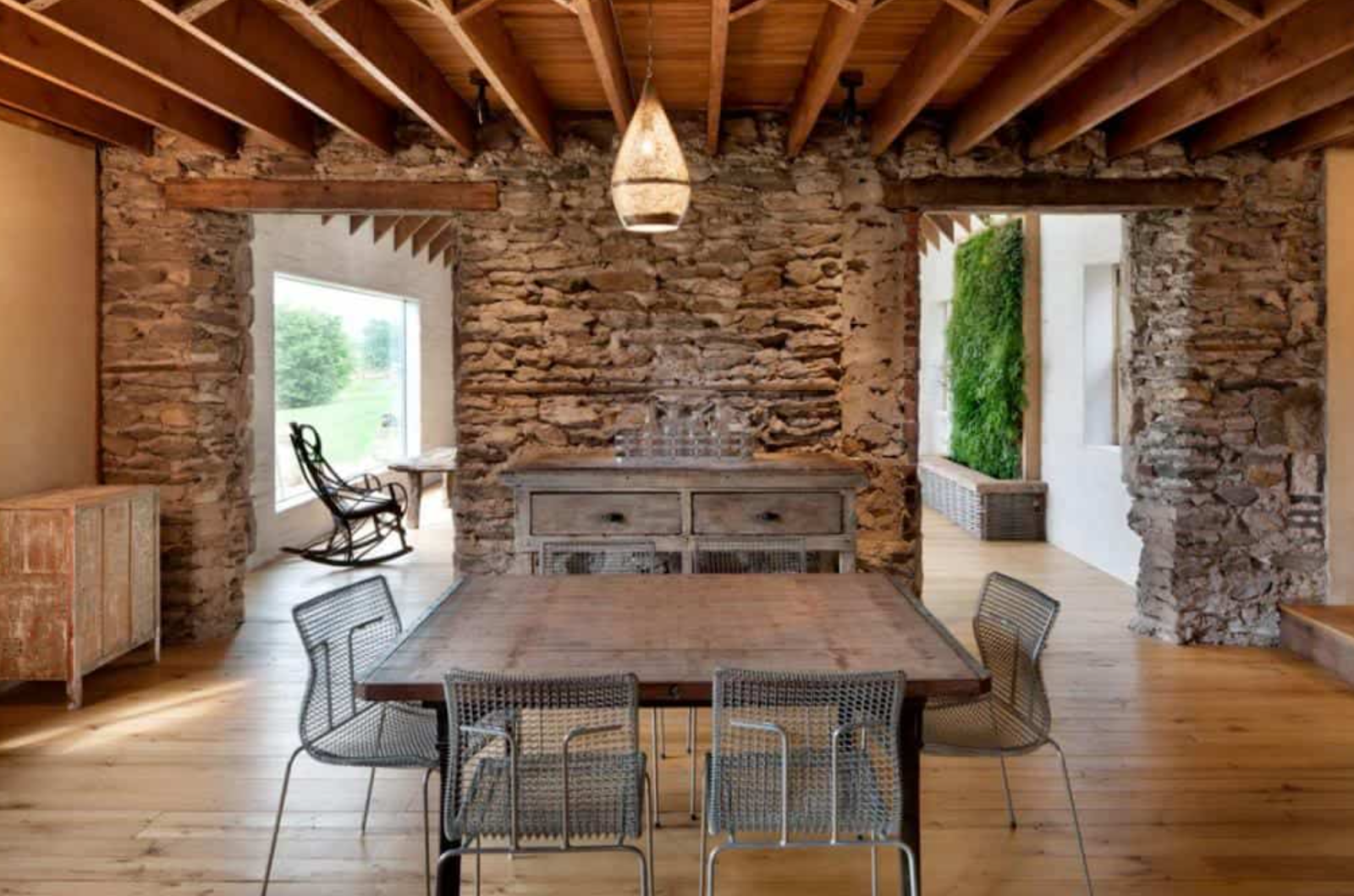 Historical barn home with exposed beams, original scraped hardwood floors, stacked stone walls, living plant wall, biophilic interior design