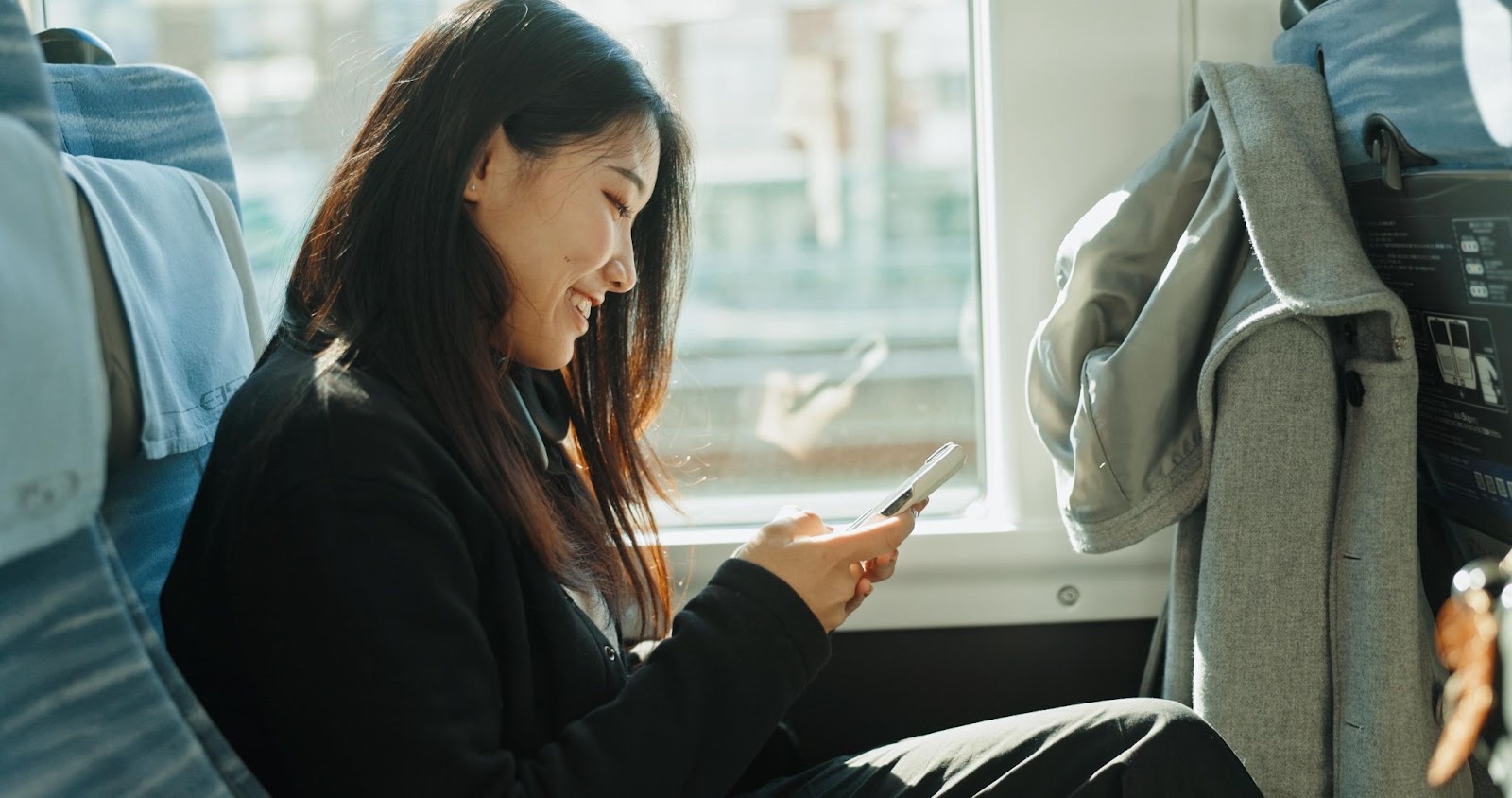 Jovem mulher sentada em um ônibus sorrindo para o celular.