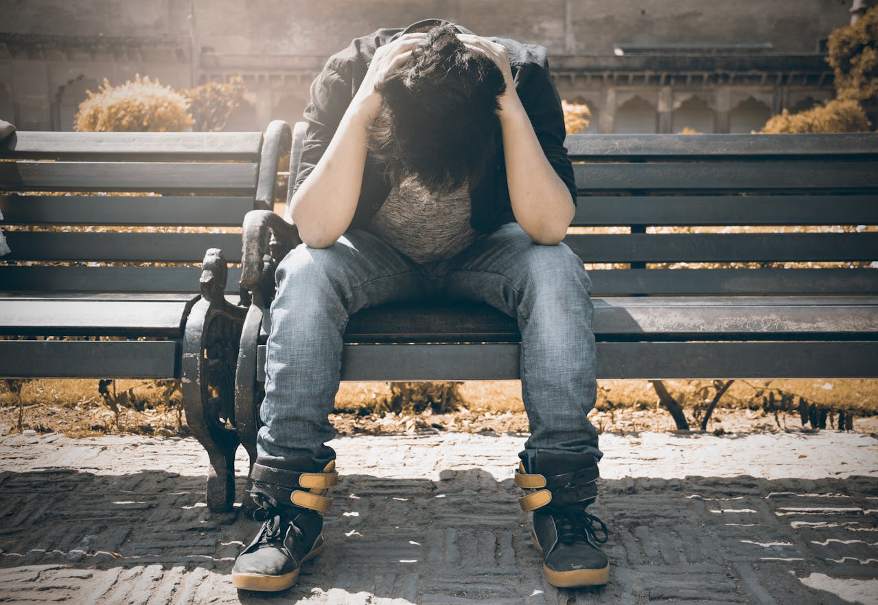 A person sitting on a bench with head in hands, looking distressed.